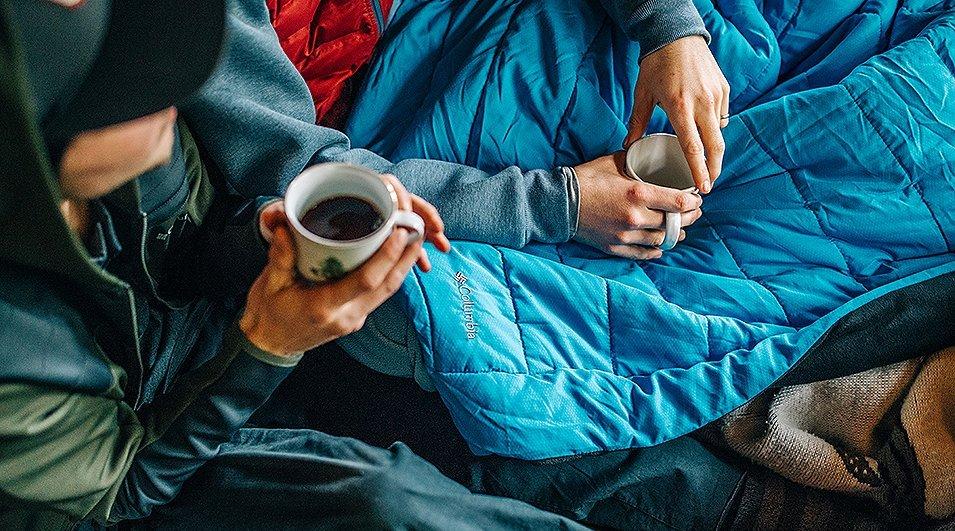 Friends drinking from coffee mugs in blankets.