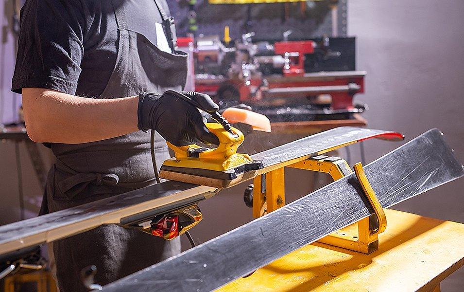 A man irons wax onto a set of skis in a garage-style workshop. 