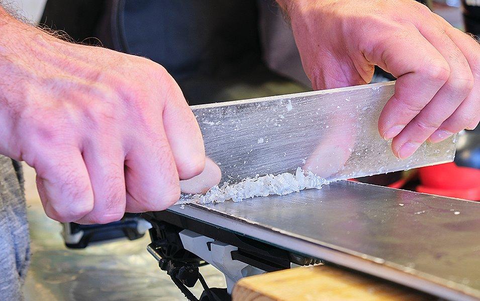 A close-up shot of a skier’s hands scraping wax off a set of skis. 