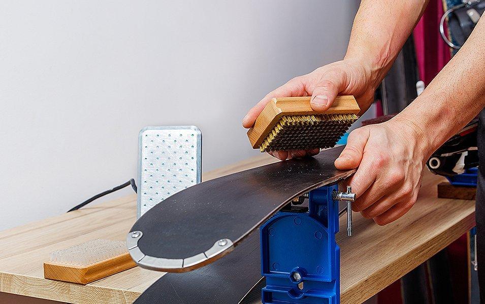 A pair of hands are pictured brushing wax off of a set of skis. 