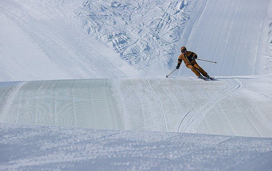 A man in an orange jacket skis down a patch of corduroy on a freshly groomed ski slope. 