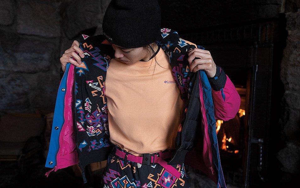 A person shows the layers of a vibrantly patterned Columbia Sportswear jacket and snow pants set. 