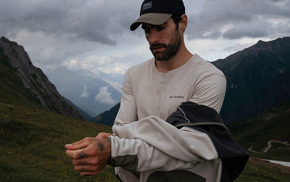 Man removing a Columbia fleece midlayer jacket on a mountain trail. 