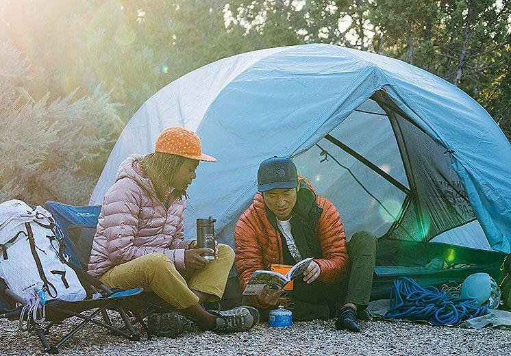 At camp, a couple looks at the map of future adventure, the female wearing the featured Rhea Ridge jacket.