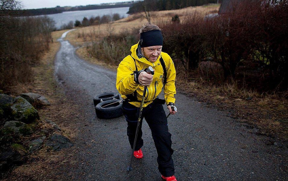 Endurance athlete Thor Hesselberg hikes through a patch of brush carrying hiking poles and towing a fitness sled made out of tires.  