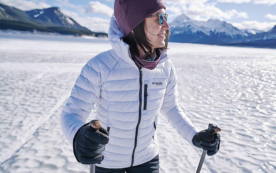 Woman in a Columbia puffy jacket walks with poles across icy ground.