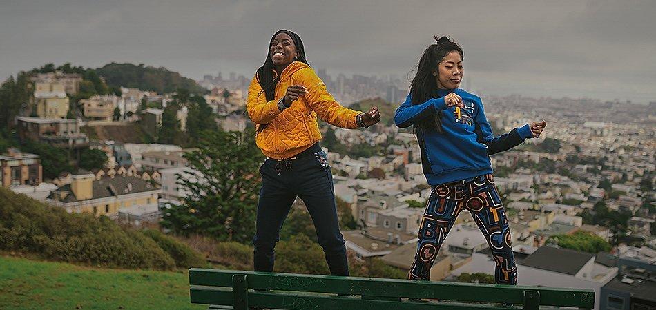 Two women dancing on a park bench overlooking a city.