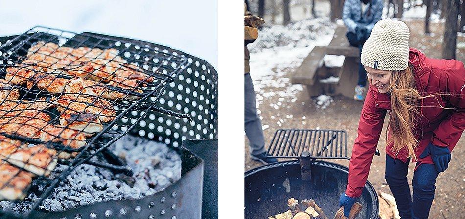 Food on a grill. A woman in Columbia gear adding wood to an outdoor grill.