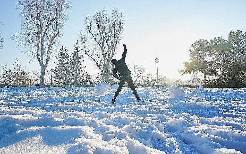 A man trains for cross country skiing in the winter by doing stretches in a snow-covered park.