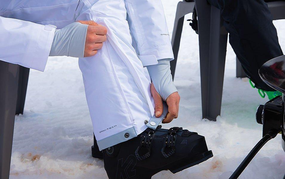 A close-up shot of a skier’s hands snapping their ski pants togeher above the boot.  
