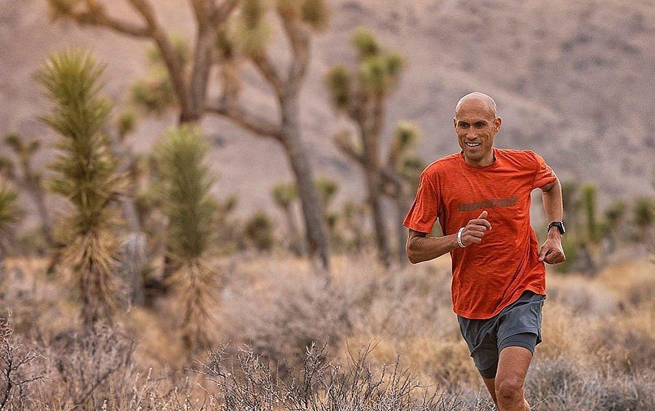 Professional athlete Yassine Diboun runs through the high desert with a smile on his face wearing a red Montrail shirt. 
