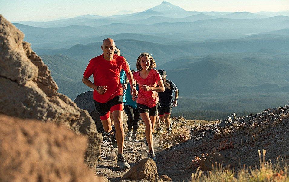 Professional athlete Yassine Diboun leads a group of runners as they climb a hill toward the camera on a beautiful day with mountains in the background.