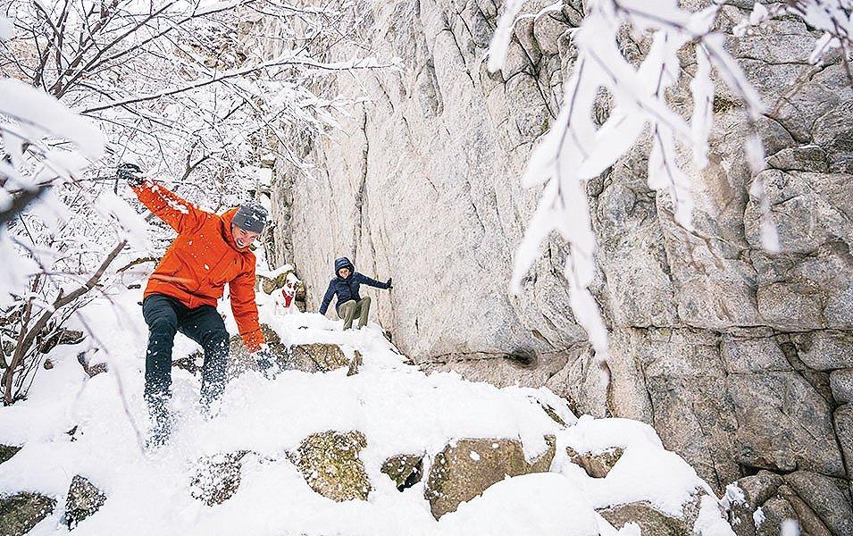 Two people scrambling down a snowy rocky slope. 