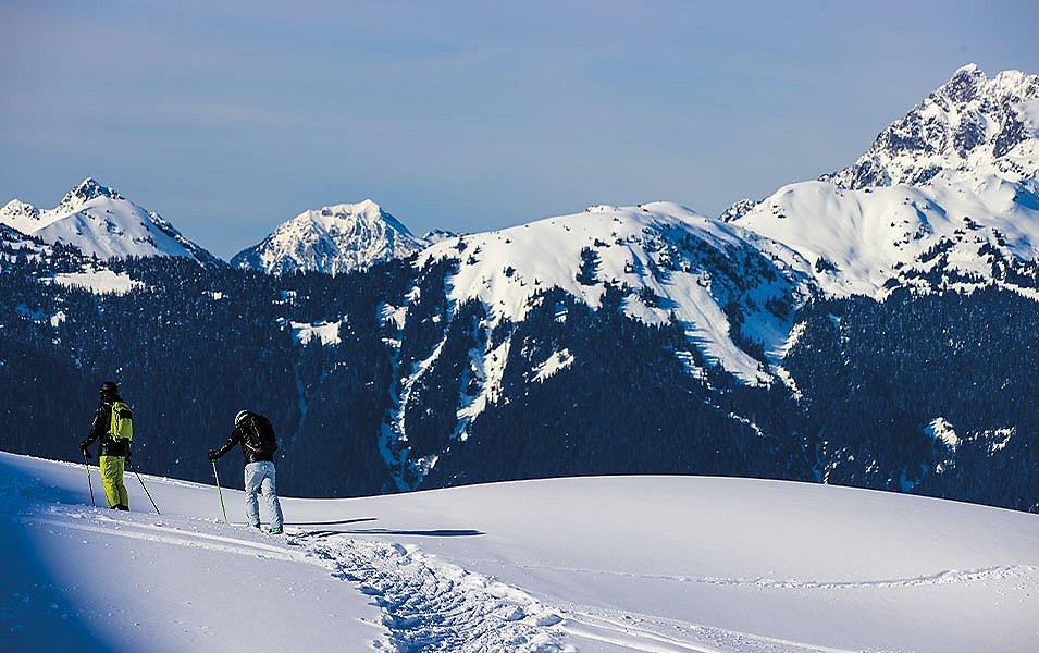 People cross country skier across a field in a snowy mountain range. 