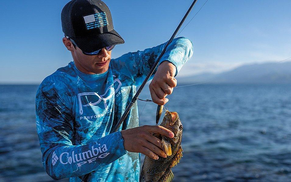 A man with a Columbia PFG sun shirt carefully removes a hook from a fish's gills.