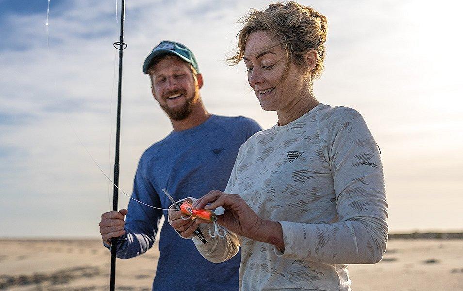 A man is holding a fishing rod while a woman is attaching an artificial lure to the line.