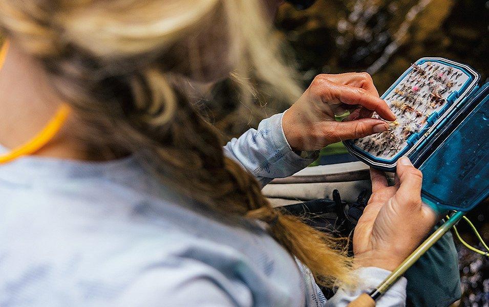 A woman looks through a carefully organized box of fishing flies.