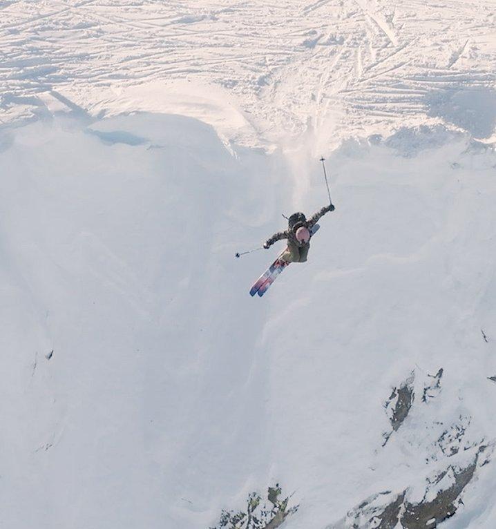 Lily free skiing off a partially snowy rockface.