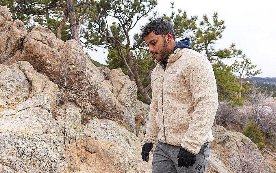 A man walks on a rocky trail wearing a white fleece jacket and black gloves. 