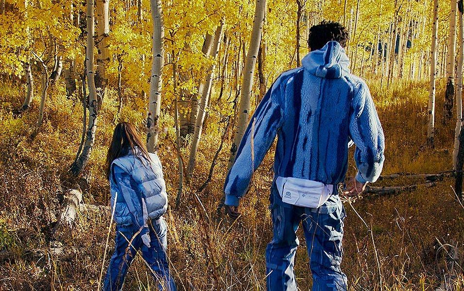 A man and a woman walk away from the camera in a scenic wooded area wearing Madhappy apparel. 