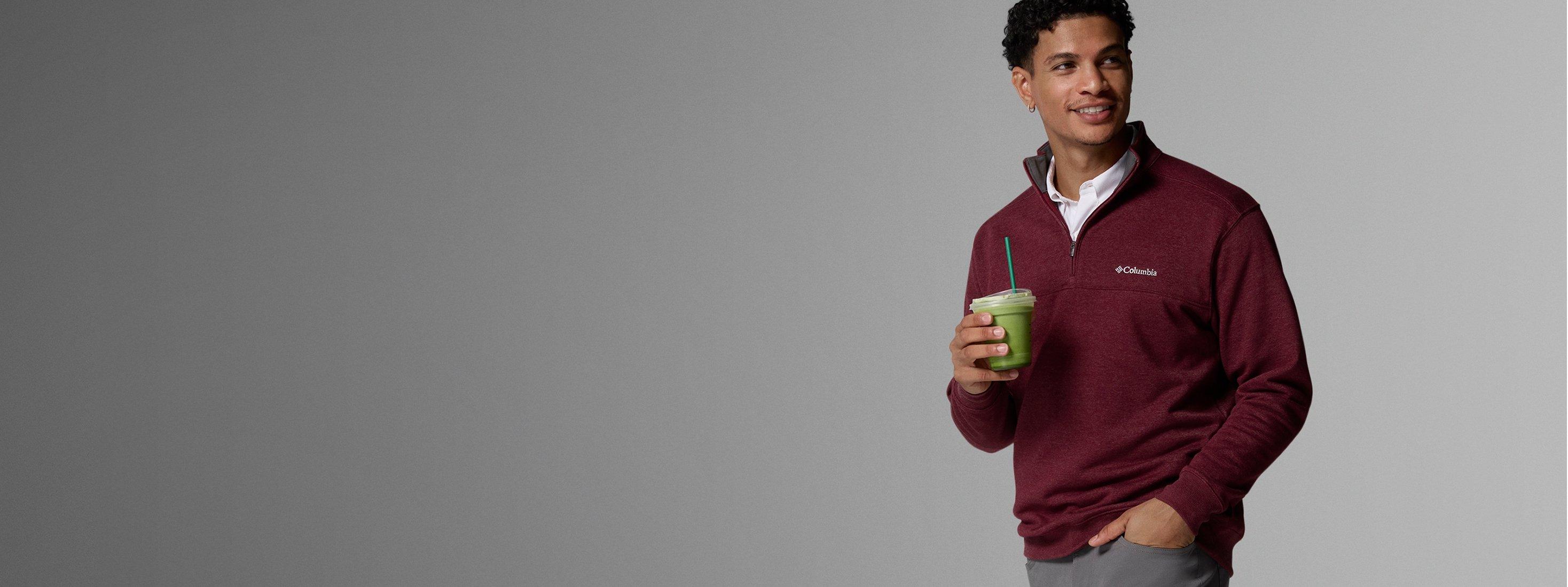 A man wearing a red quarter zip and holding an iced matcha.
