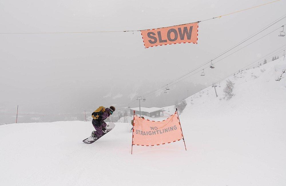 Skiing right by a SLOW sign at a ski resort.
