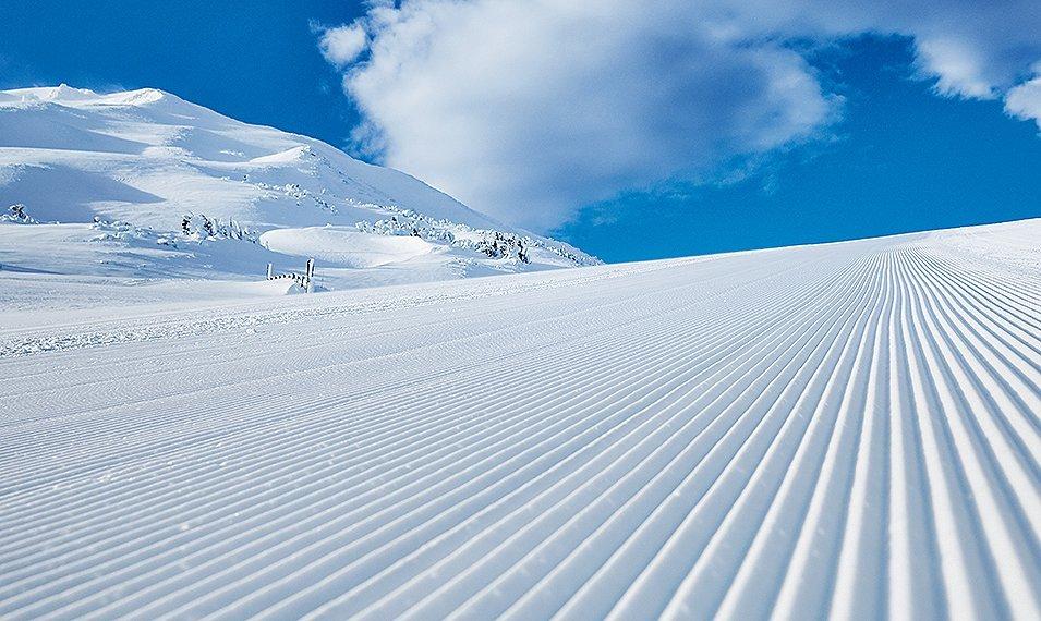 A groomed mountain ski run on a sunny day.