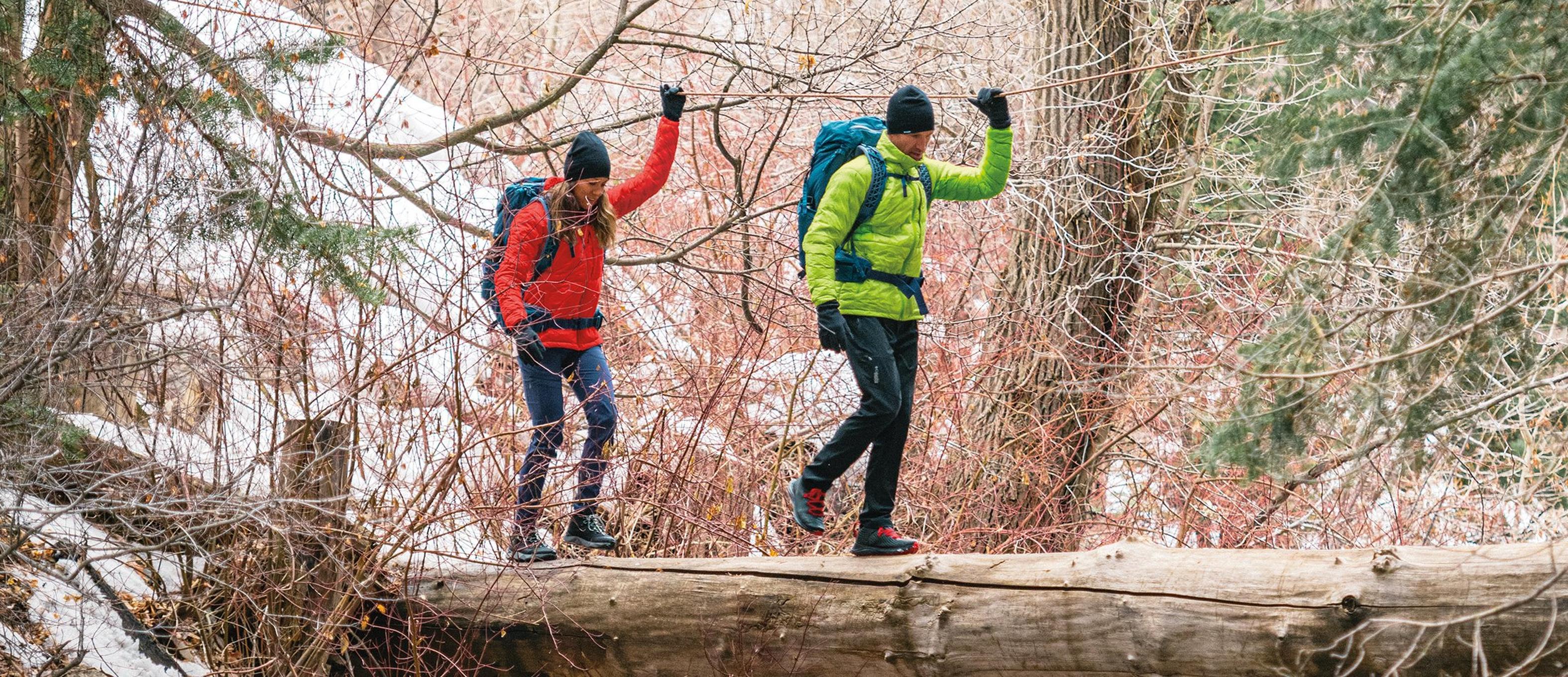 Two people in down jackets balancing across a log bridge