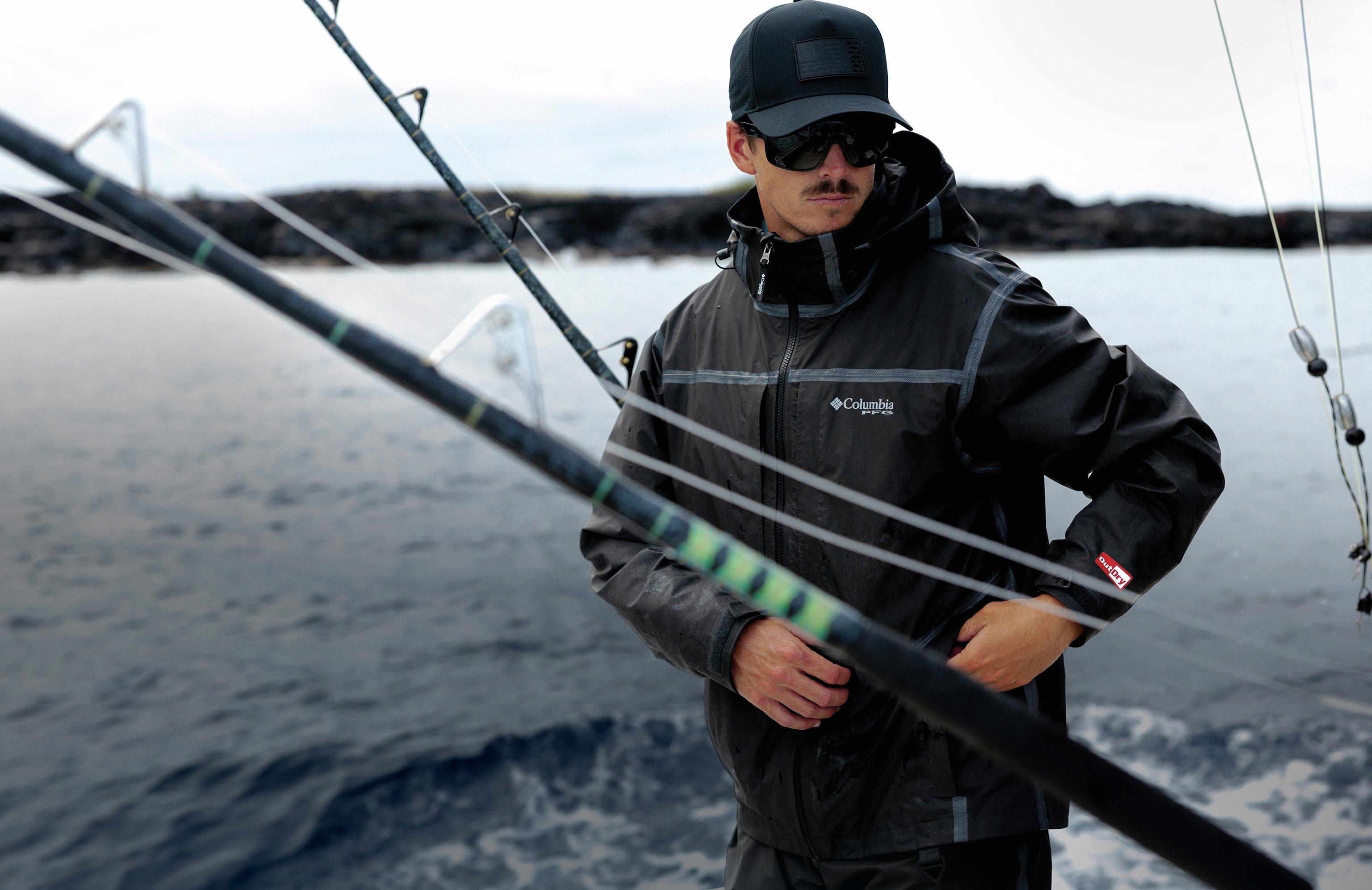 Person wearing a dark waterproof jacket and cap, standing on a boat with fishing rods visible.