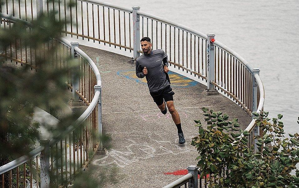 A runner rounds a corner on a waterside trail, leaning in to maintain balance and traction as he accelerates.