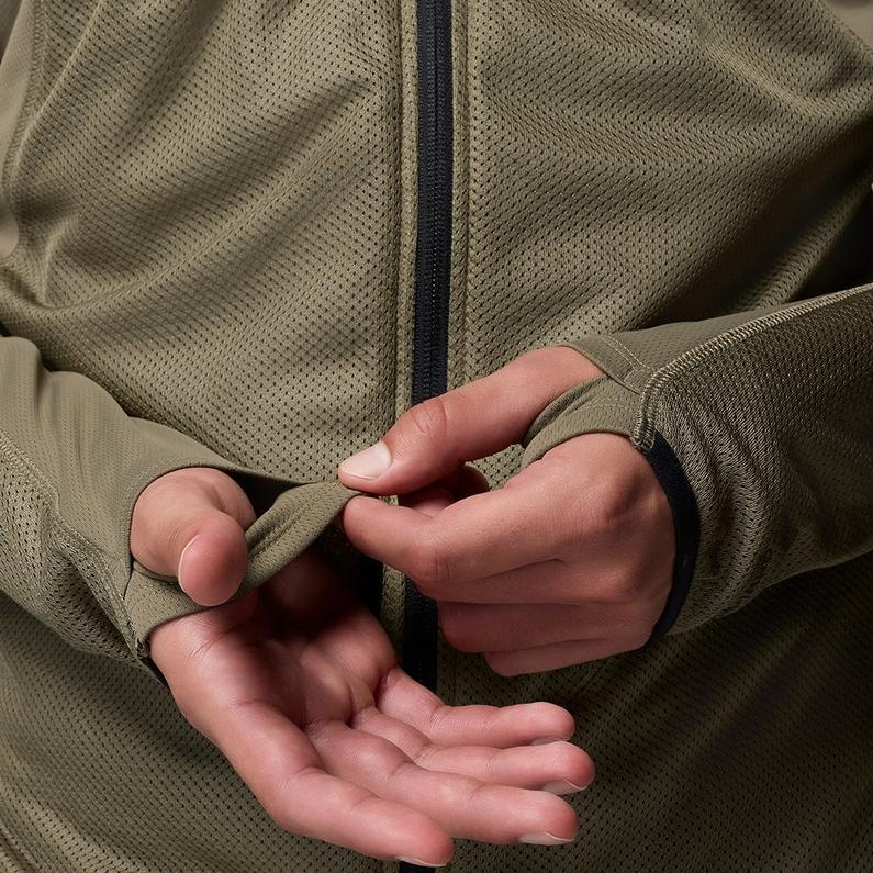 A man adjusting the thumbholes on the extended sleeves of his green top.