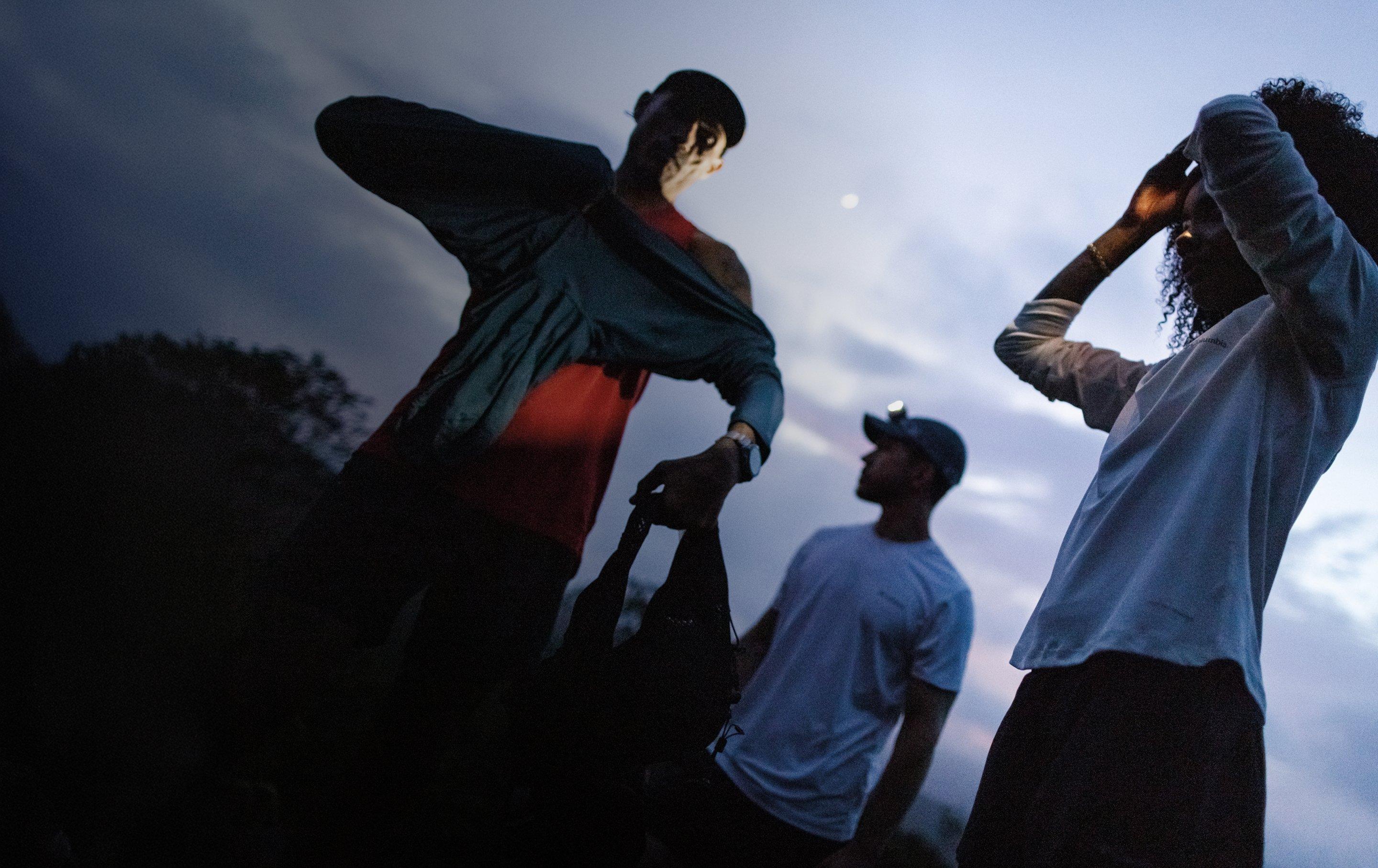 People in casual clothing looking up at the night sky, with one person holding what appears to be a camera.