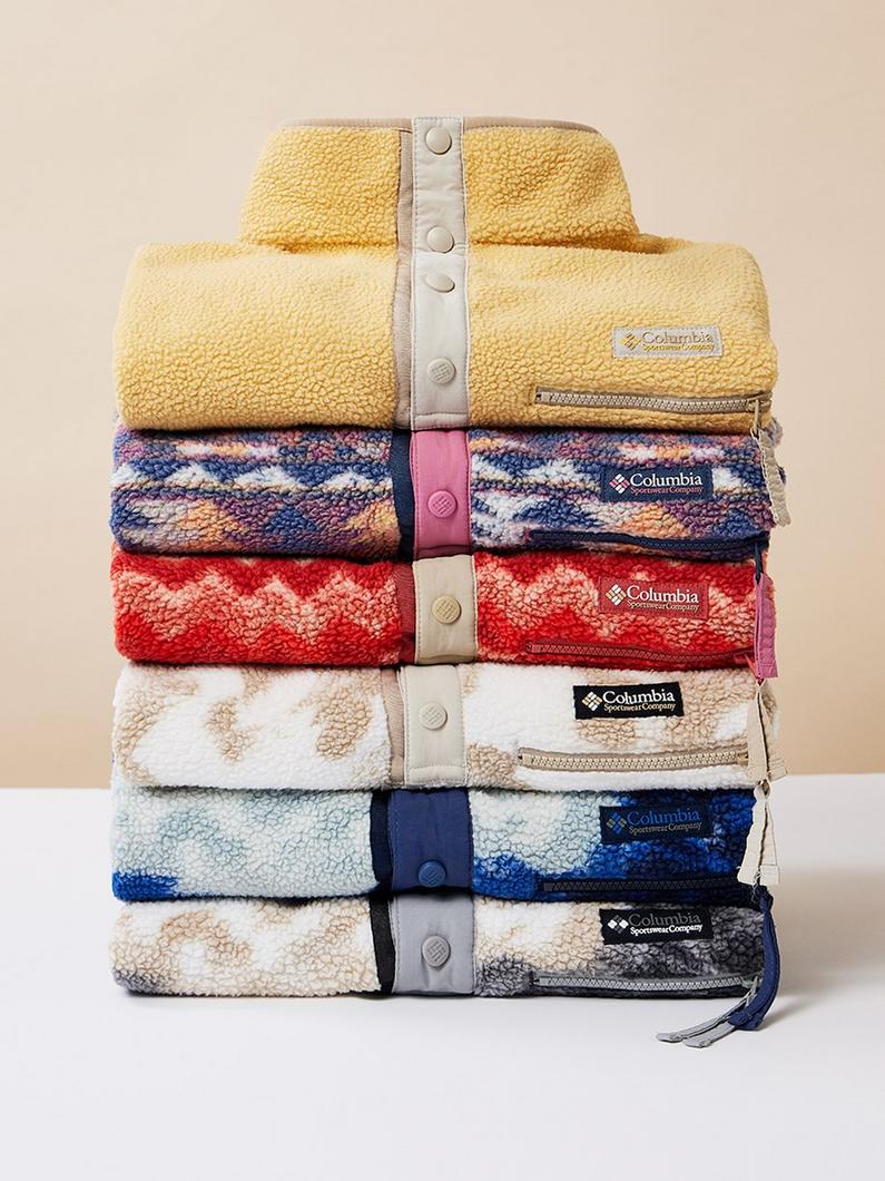 Stack of six folded fleece pullovers in various colors with snap closures and zippered pockets.