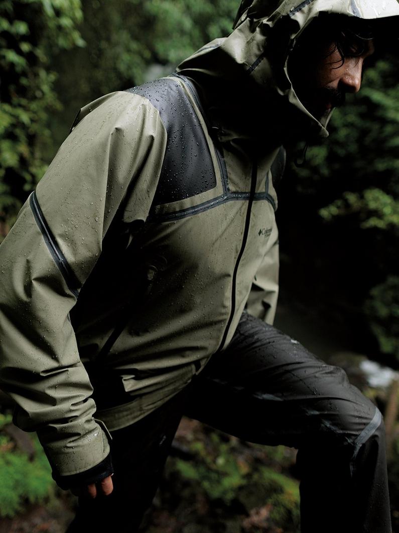 A man hiking in a rainy forest, wearing a dark green rain jacket.