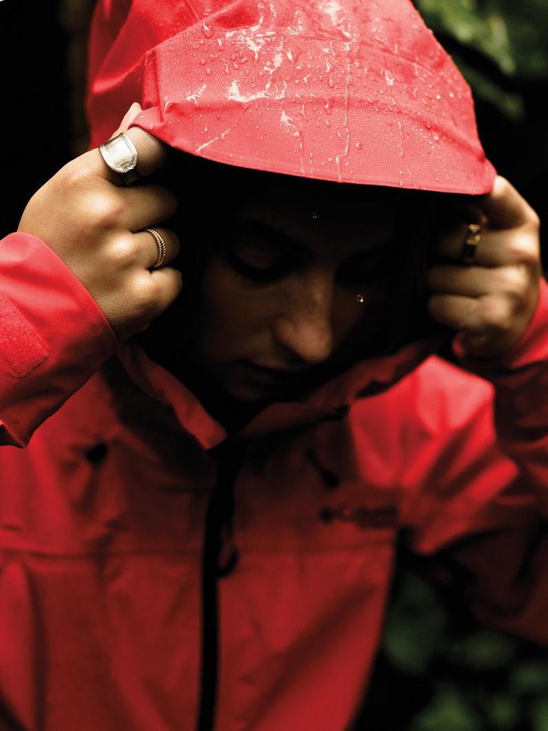 A woman putting up their hood on a red waterproof jacket in the pouring rain.