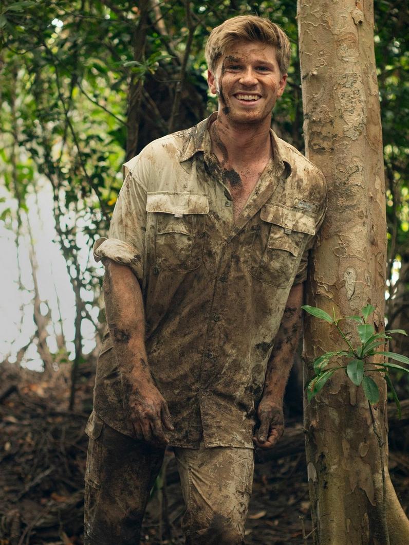 Columbia ambassador Robert Irwin in Columbia gear in a jungle, covered in mud.