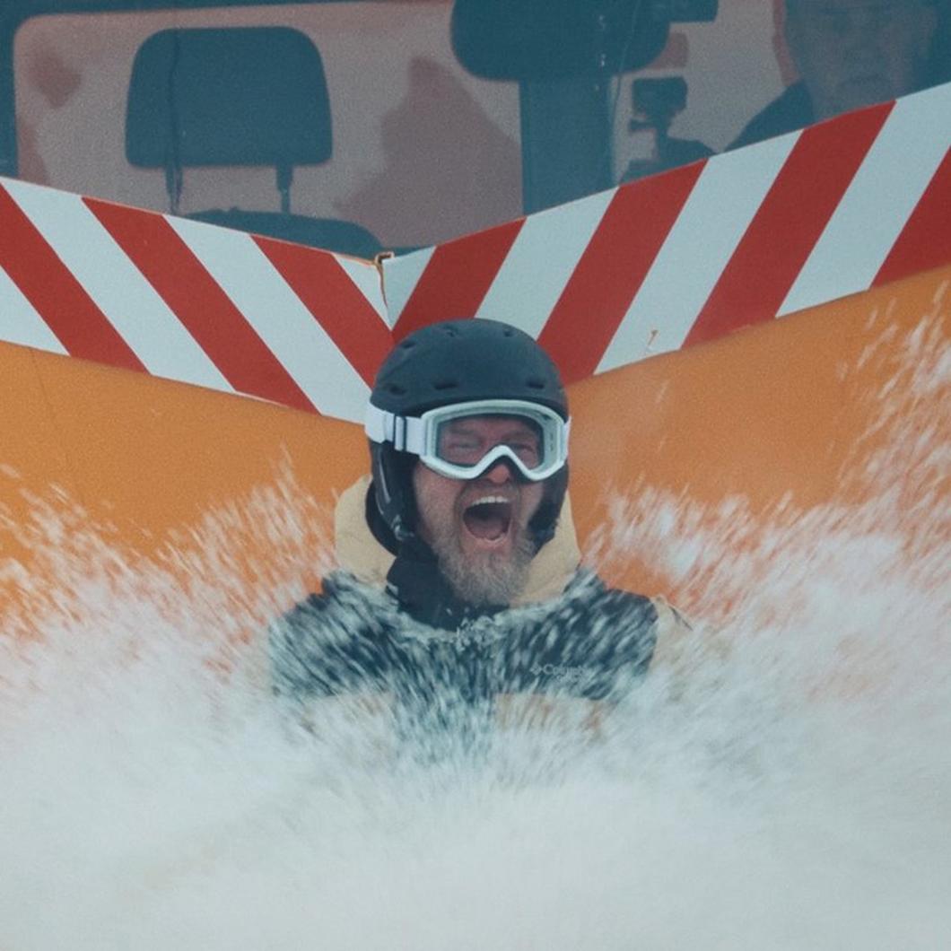A stunt man strapped to a snow plow living his best life.