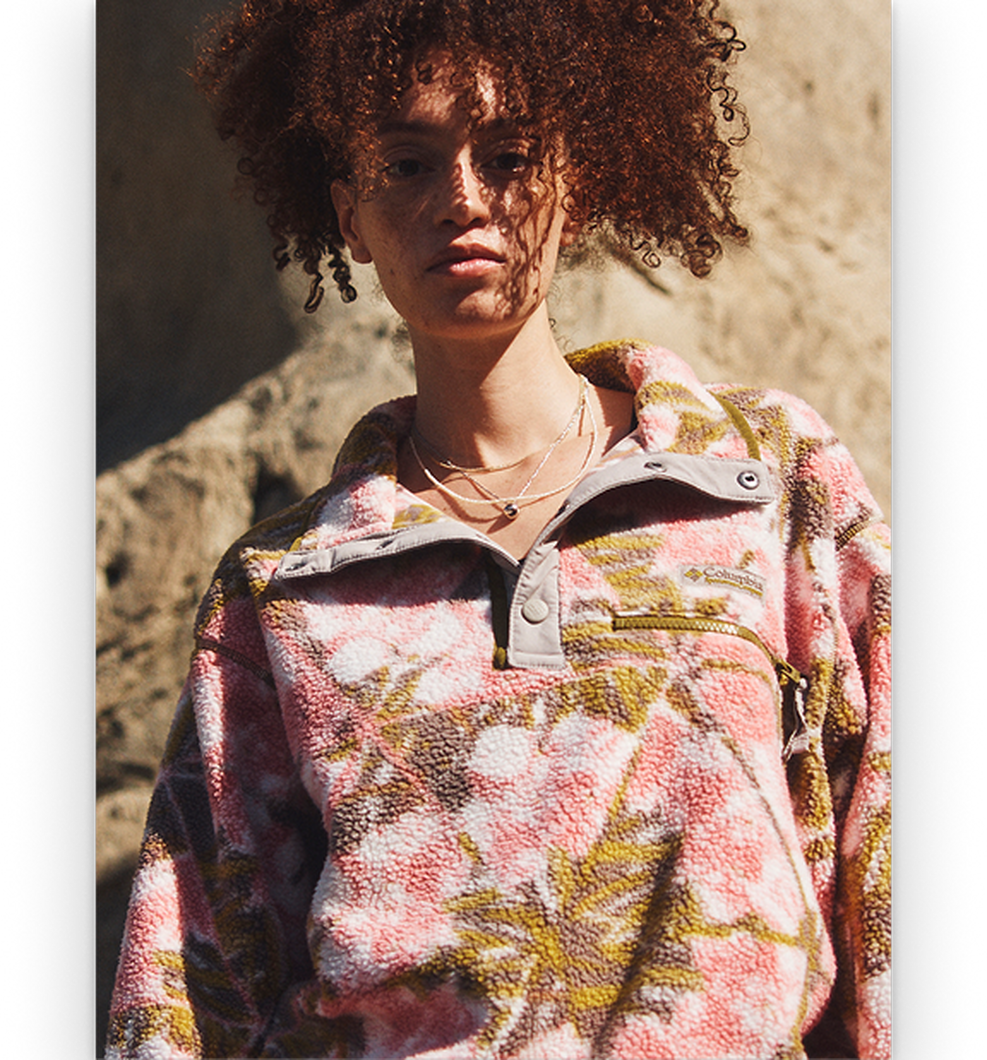 Woman wearing a pink, white, and gold patterned fleece pullover with layered necklaces.