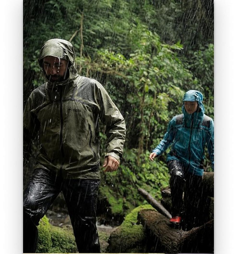 Two hikers in rain gear trekking through a wet forest in heavy rainfall.