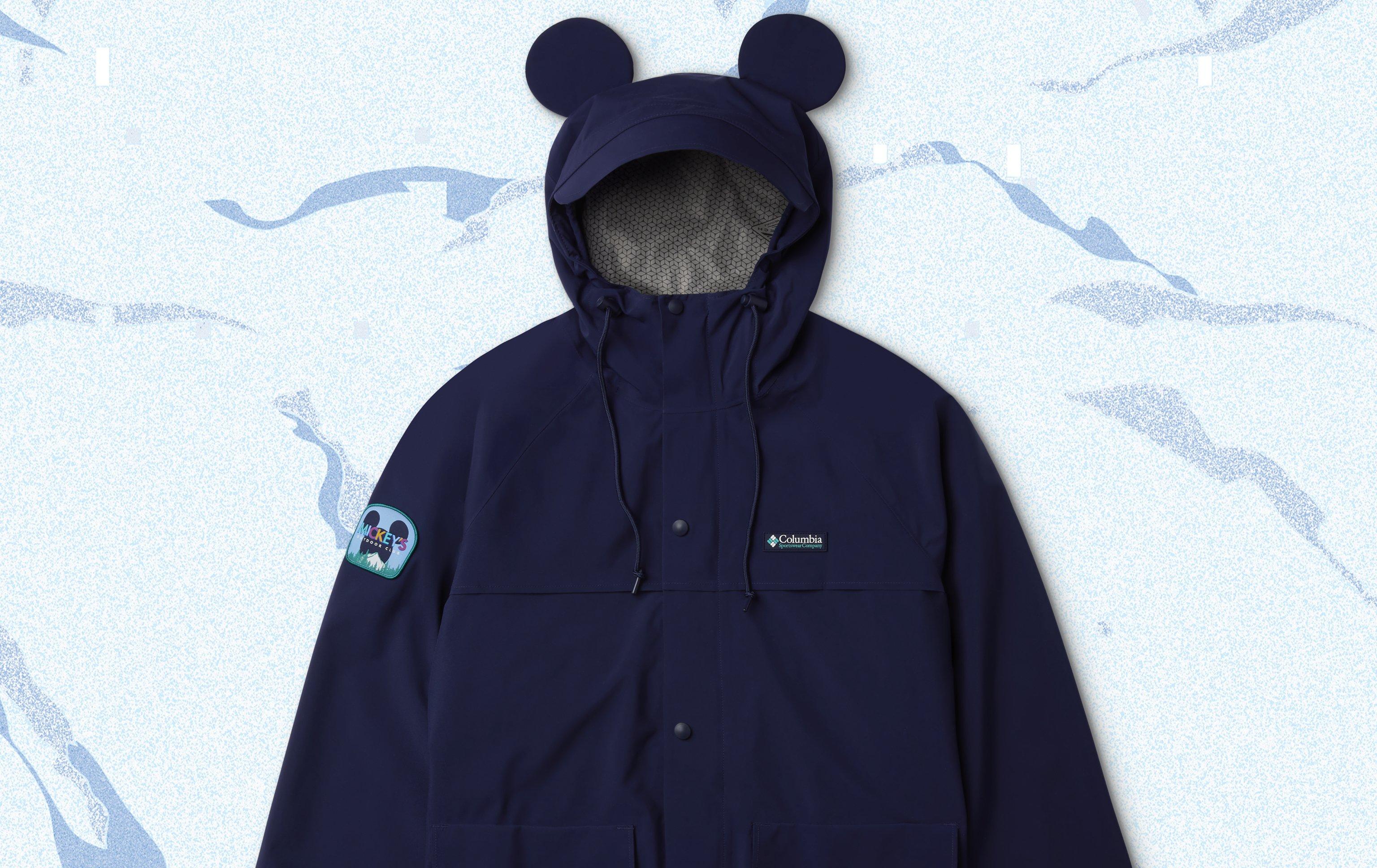 Product lay down of a jacket with Mickey Ears over a snowy backdrop with illustrated trees.