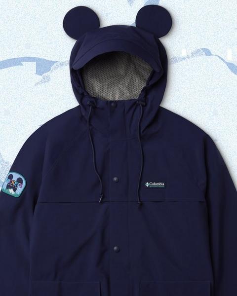 Product lay down of a jacket with Mickey Ears over a snowy backdrop with illustrated trees.