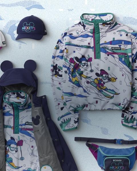Product lay down of fleece, jackets, and accessories over a snowy backdrop with illustrated trees.