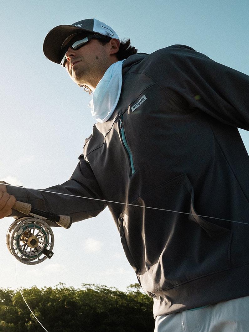 Man reeling in a fish with a sun flare in the center of the image.