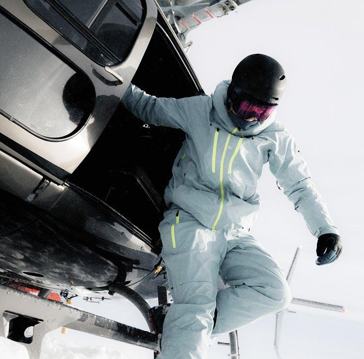 A skier in head to toe gear about to jump out of a helicopter.
