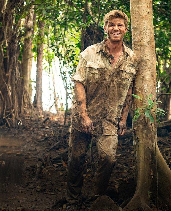 Robert Irwin covered in mud in a wild forest.
