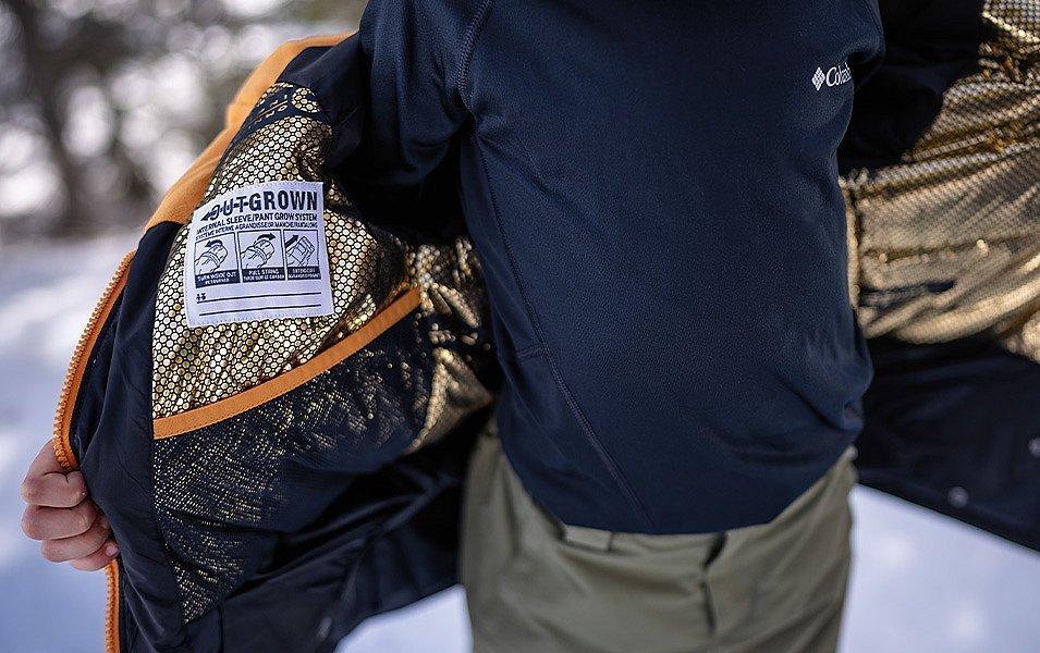 A person wearing an Outgrown jacket holds it open to reveal the inside label, which provides easy instructions for extending the sleeve length.