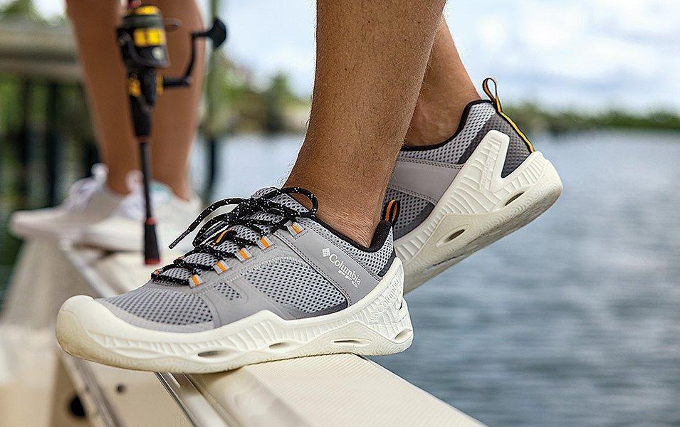 A person wearing Columbia PFG shoes with biomimicry-inspired soles maintains a steady balance on the slippery rail of a fishing boat.
