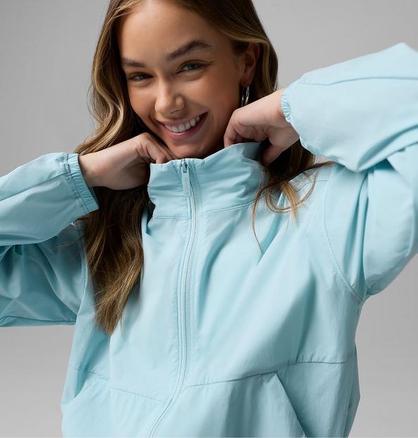 Person smiling while zipping up a light blue athletic jacket with elastic cuffs and hood.