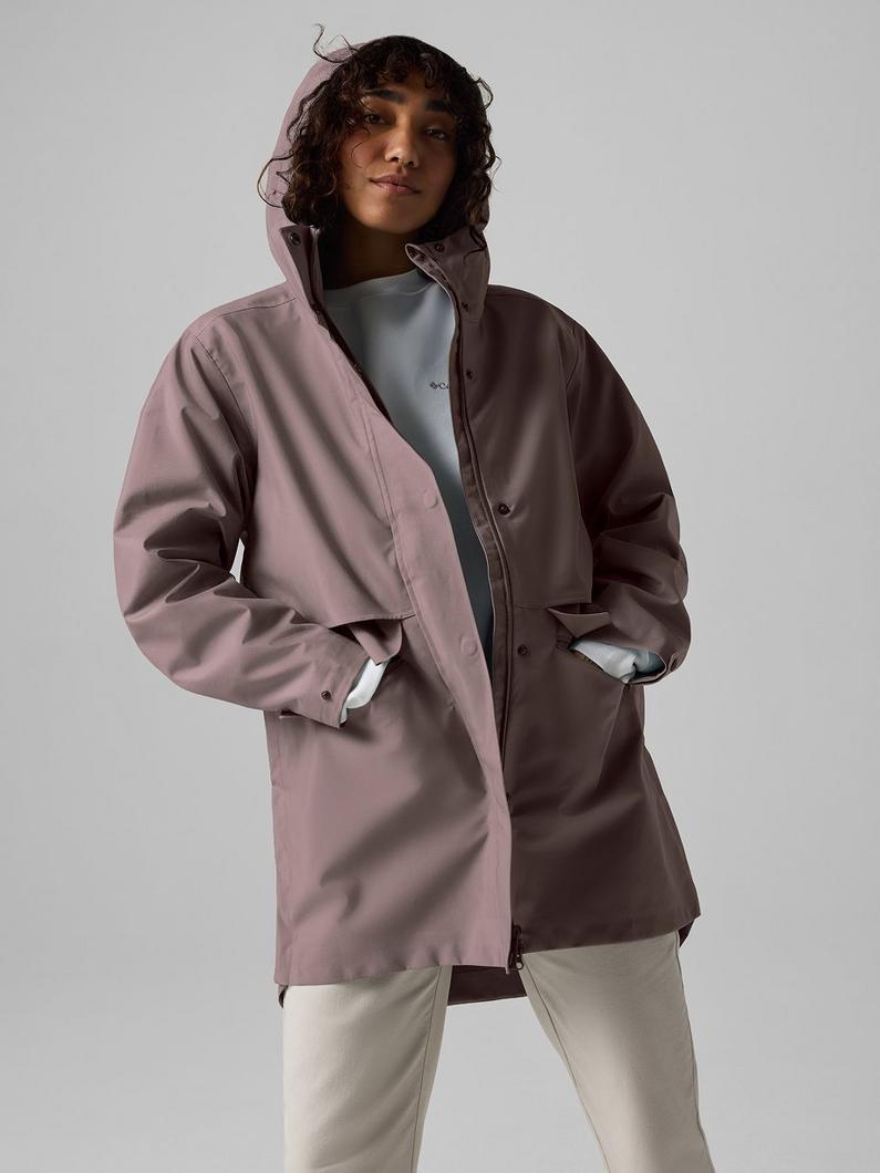 A woman wearing the taupe rain jacket with the hood up.