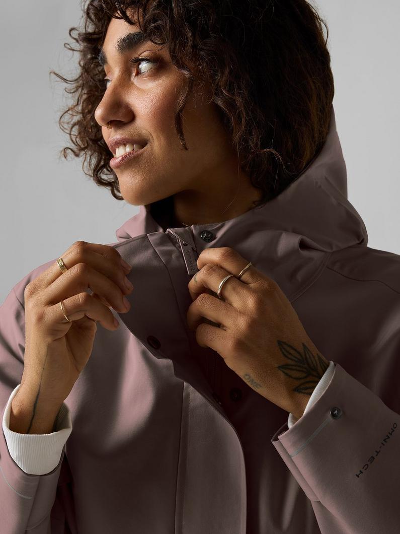 A woman wearing the taupe rain jacket with the hood up.